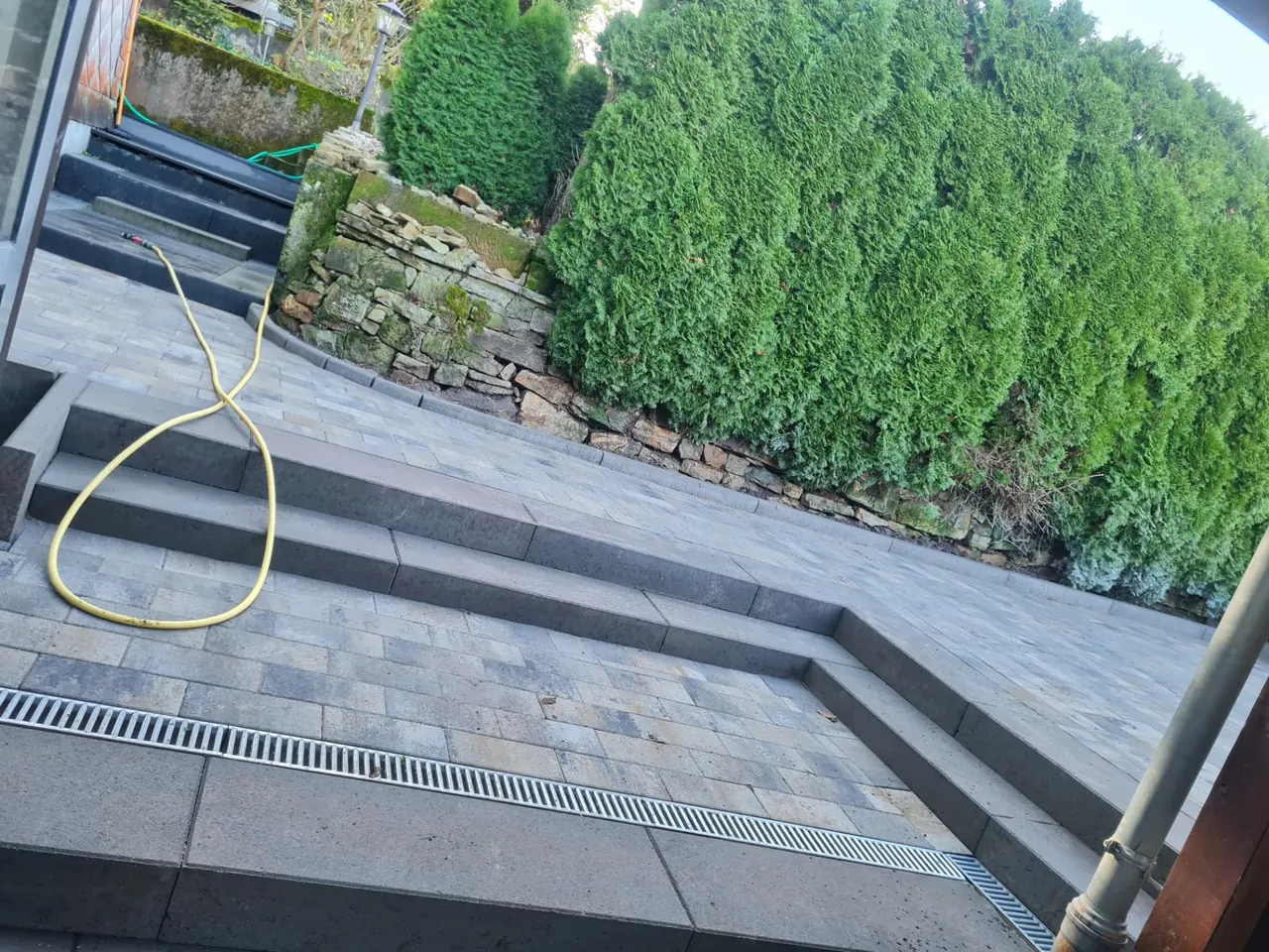 Moderne Terrasse mit großformatigen grauen Platten, Stufen und Entwässerungsrinne